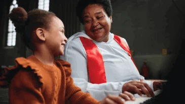 A woman teaching little girl to play piano during performance in church