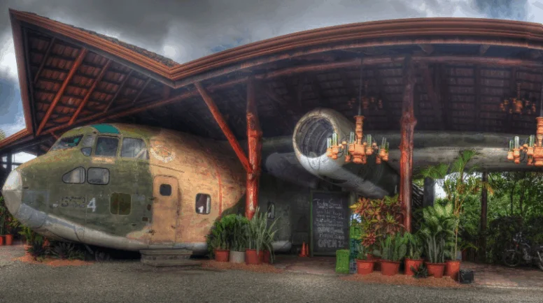 An old airplane with a tin roof over it and restaurant tables around it