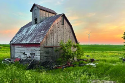 Wooden barn on a field with a windmill in the distance.
