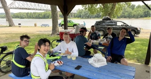A group of young men eat at picnic tables.