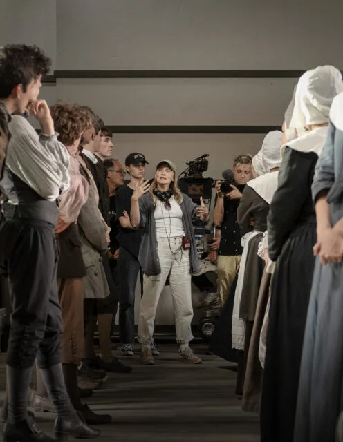 Director Mona Fastvold, center, with cast and crew on the set of “The Testament of Ann Lee." (Photo © 2025 Searchlight Pictures)