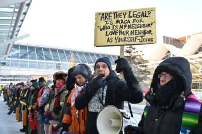 Faith leaders demonstrate against ICE tactics. One holds the sign "'Are they legal?' Is MAGA for 'Who is my neighbor?' Love your neighbor as yourself — Jesus"
