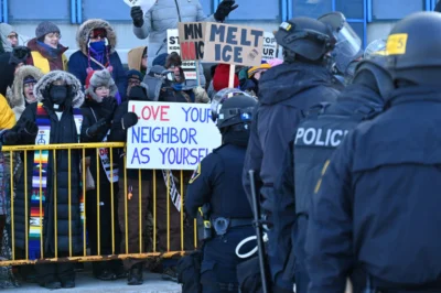 Police stand in front of protesters, including one holding a sign "love your neighbor as your self"
