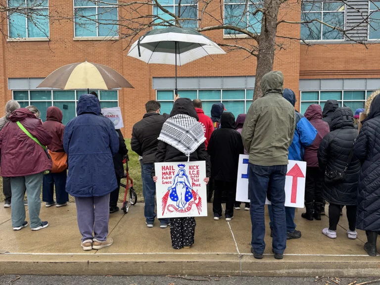 A group in winter coats with umbrellas and signs stands outside.
