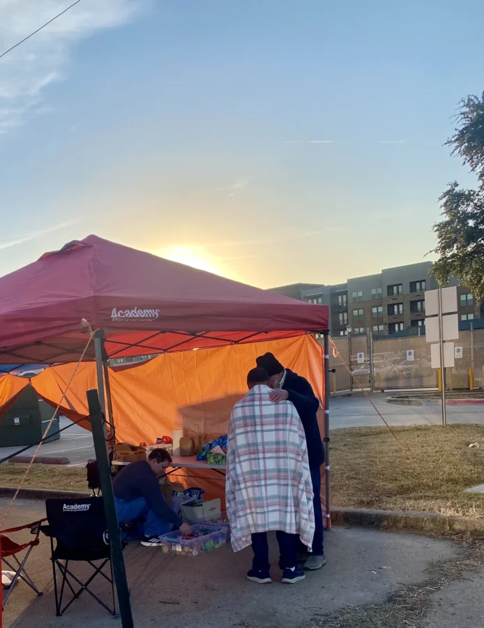 A woman wrapped in a blanket speaks to someone under a red canopy tent located outside of the ICE detention center in Dallas.