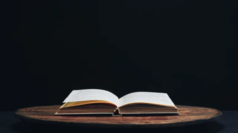 One open old book on a round wooden table. Beautiful dark background.