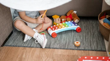 A toddler sits in a fort with toys.