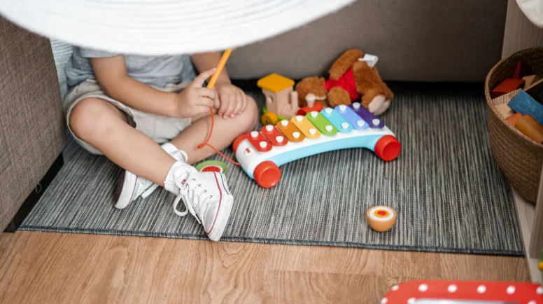 A toddler sits in a fort with toys.