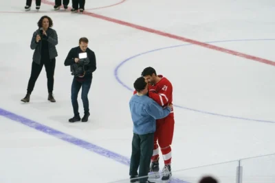 Two men kiss on the ice of a hockey arena. One is a hockey player.