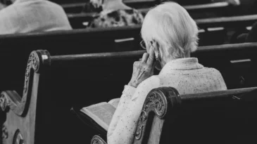 An elderly woman sits in a church pew reading her Bible