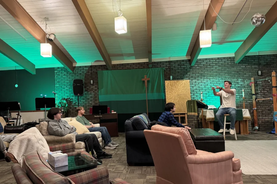 A pastor sits on a stool and students sit on couches