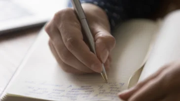 Hands of woman taking notes of online lecture webinar in notebook. Student, author, writer writing on paper page of journal or diary, holding pen, preparing text, making memo for article. Close up