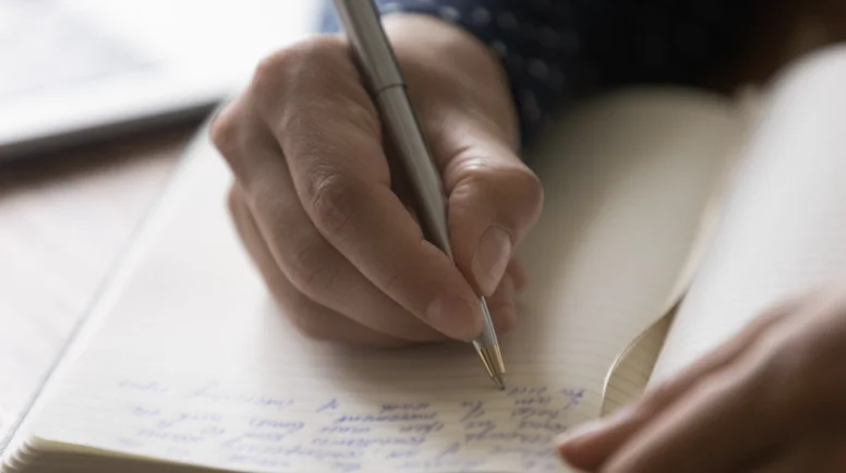 Hands of woman taking notes of online lecture webinar in notebook. Student, author, writer writing on paper page of journal or diary, holding pen, preparing text, making memo for article. Close up