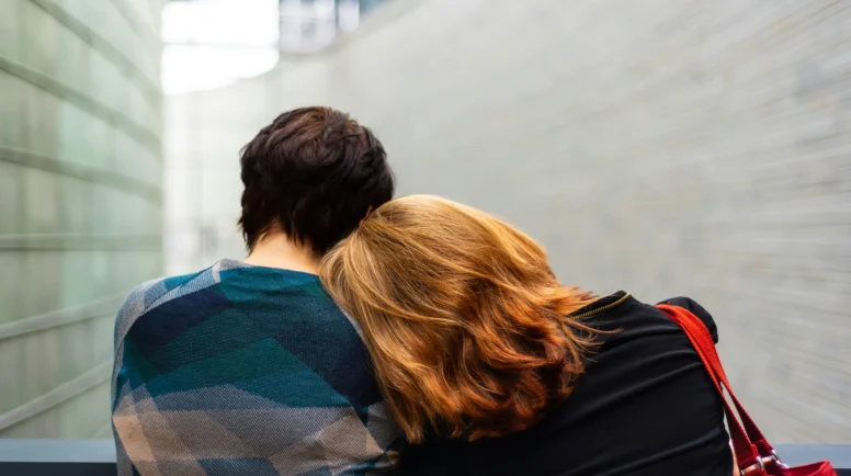 A Woman with red hair resting her head on a male loved one with dark hair