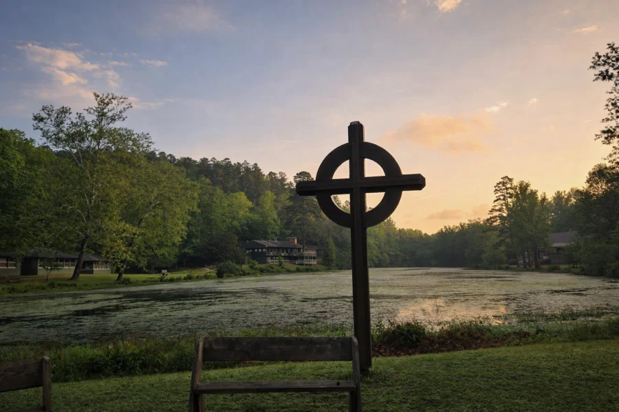 A cross in the foreground and a pond and sunset in the background