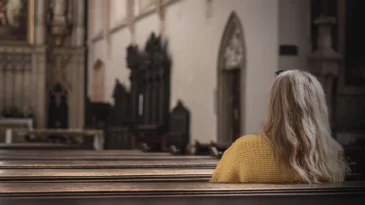 Woman sitting on pew and praying in empty church. Catholic religion at European culture. Faith and hope concept