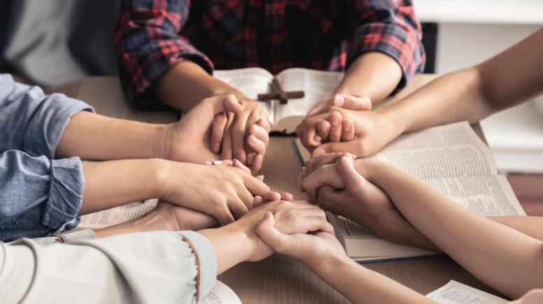 Cropped image of diversity people hand praying together at wooden church on bible book while hold hand together with believe. Concept of hope, religion, faith, god blessing concept. Burgeoning.