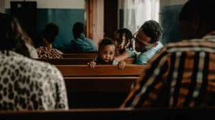 A toddler turns around in a church pew while everyone else is facing the front of the sanctuary