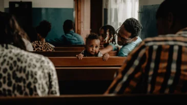 A toddler turns around in a church pew while everyone else is facing the front of the sanctuary