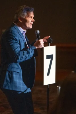 A man in a blue suit stands behind a microphone.