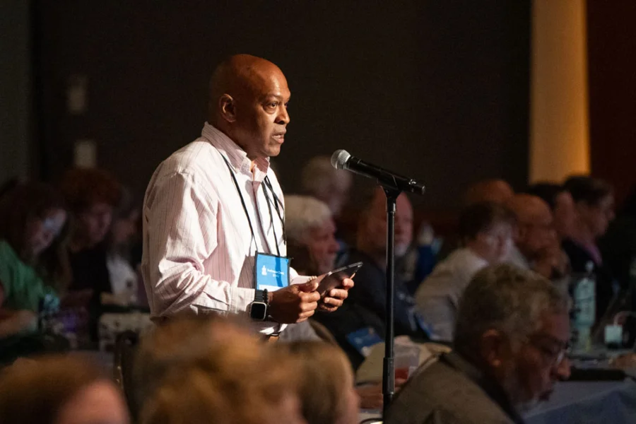 A man stands behind a microphone with his phone in his hand.