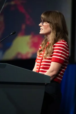 A woman stands behind a podium with the PC(USA) logo.