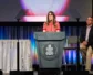 A woman stands behind a podium with the PC(USA) logo.