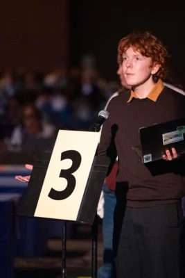 A young man stands behind a microphone with a laptop in his hand.