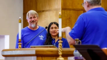 Mark Adams and Miriam Maldonado stand, arm in arm, in front of Tony Larson as he speaks to them.