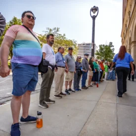 A group of people stand hand in hand in front of the Milwaukee City Hall.