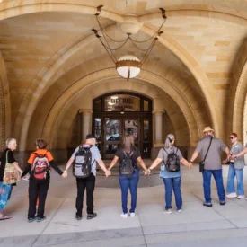 A group of people stand hand in hand in front of the Milwaukee City Hall.