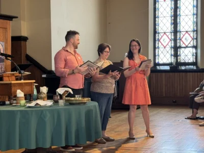 Three people stand in the front of a sanctuary with folders in hand.