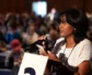 A young woman speaks that a microphone while holding her phone.