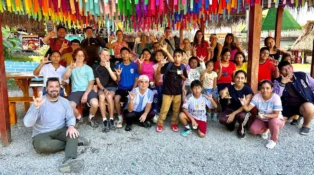 A group of children and adults pose for a picture under a pavilion with rainbow fabric hanging from the ceiling.