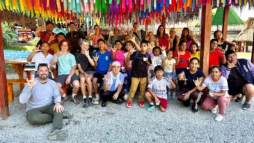 A group of children and adults pose for a picture under a pavilion with rainbow fabric hanging from the ceiling.
