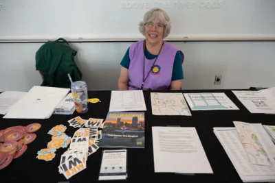 A woman in a purple vest sits behind a table with information about Milwaukee on it.