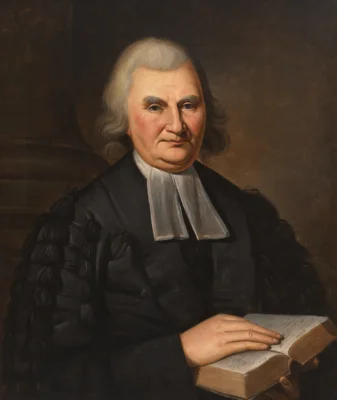 A white man in traditional Protestant pastoral garb from the 18th century, including Geneva robes and white preaching tabs.