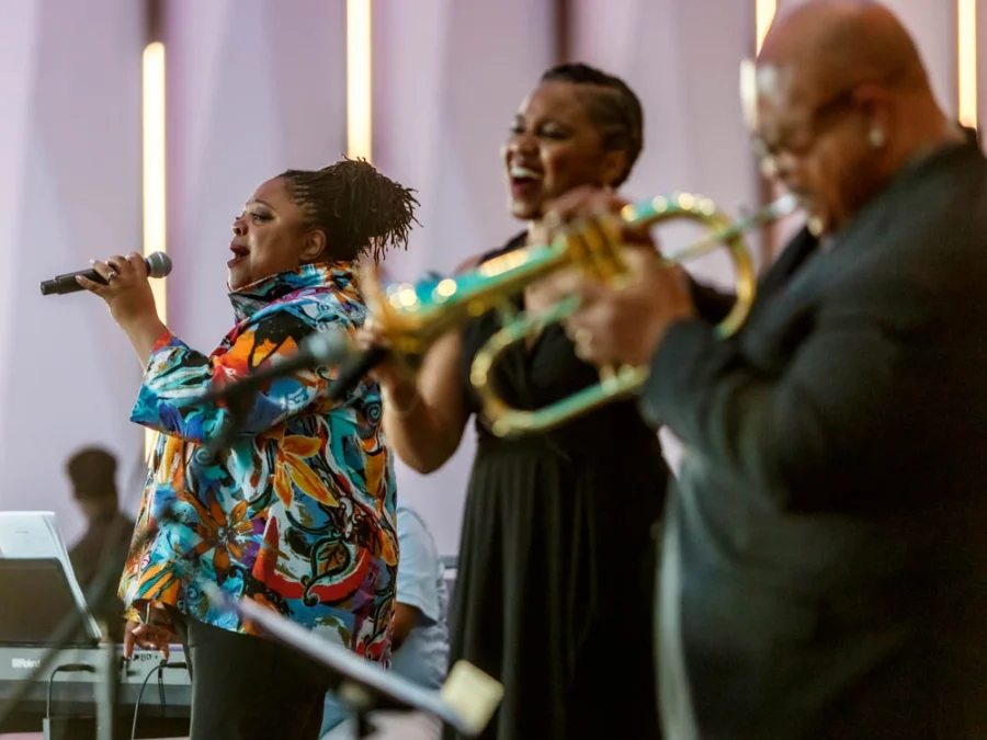 Two women sing and a man plays the trumpet