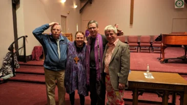 Four people with ashes on their foreheads take a picture in a church's sanctuary
