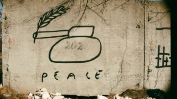 A concrete wall, during warm with a mural of a tank and written below, "peace."