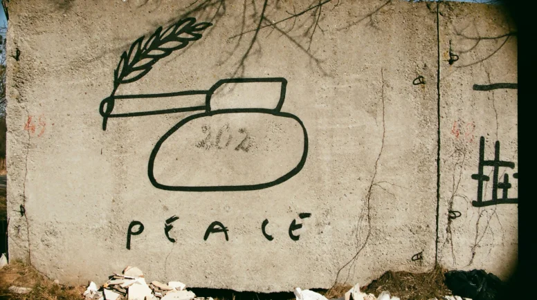A concrete wall, during warm with a mural of a tank and written below, "peace."