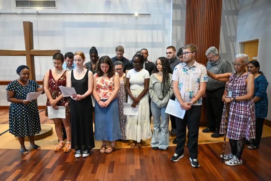 A group of young adults stand at the front of a worship space while older adults stand around them in prayer.