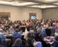 A group of people sitting in a conference room around round tables.