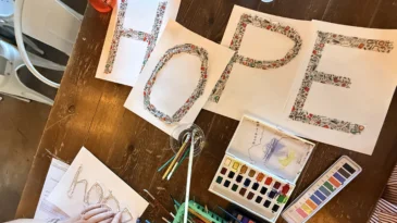 Art supplies are displayed on a table, along with four pages of paper that together say "hope."