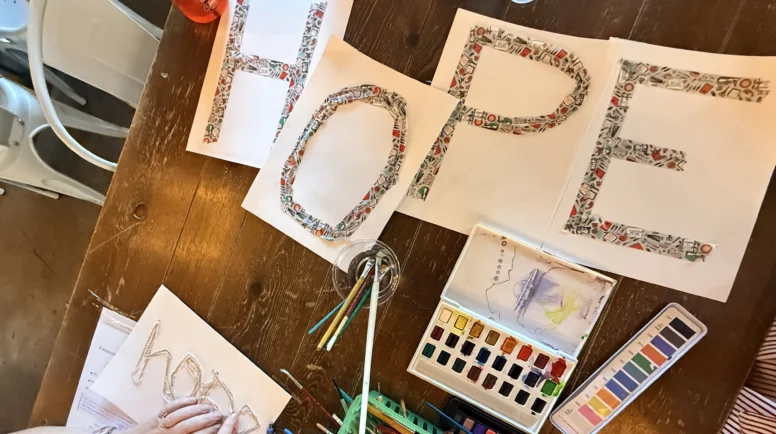 Art supplies are displayed on a table, along with four pages of paper that together say "hope."