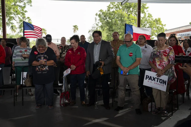 A group of people pray outside, holding Paxton signs