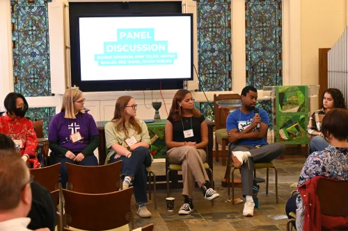 A panel of young adults sit in the front of a room.