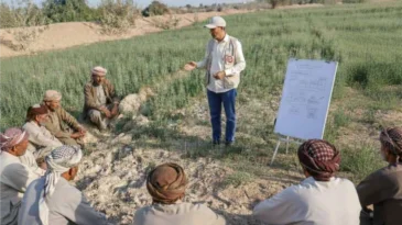 A semi-circle of men sit, listening to a man speak
