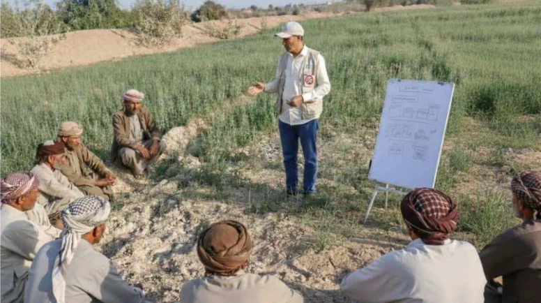 A semi-circle of men sit, listening to a man speak