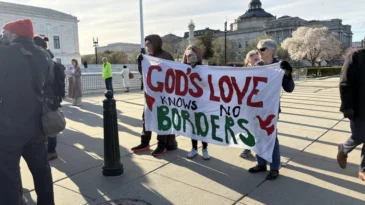 A group of people standing outside holding a sign, "God's love knows no borders"